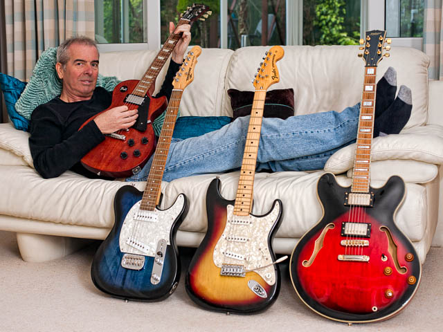 Guitarist reclining on sofa surrounded with guitar collection