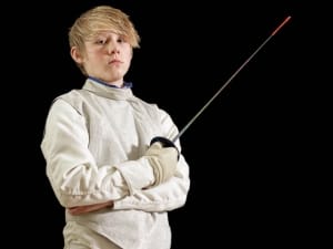 Young Male Fencer Holding Foil with Arms Crossed on Black Background