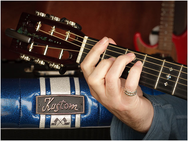 Close Up Of Guitarist With Hand On Guitar Fretboard With Amplifier in Background