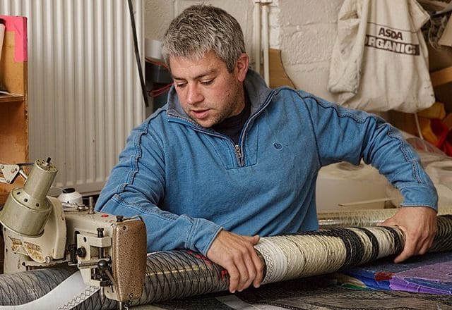 Portrait of sailmaker in workshop repairing sail with industrial sewing machine