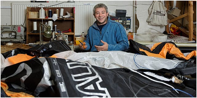 sailmaker-surrounded-by-sail-and-machinary-in-workshop Portrait Of Male Sailmaker Surrounded by Sails In His Workshop