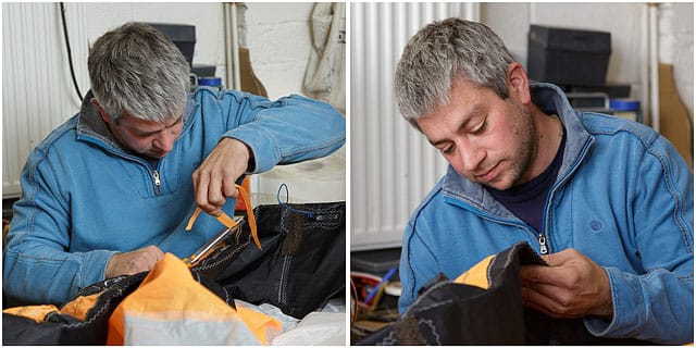 sailmaker-working-on-repairing-sails Portrait Of Male Sailmaker With Blue Top Repairing Sails By Hand In Workshop
