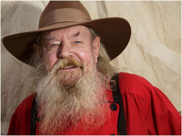 Head And Shoulders Portrait Of Man Dressed As An American Cowboy In Red Top And Brown Hat