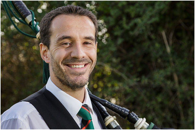 Portrait Of Male Bagpiper Standing Against Green Foliage Holding Bagpipes