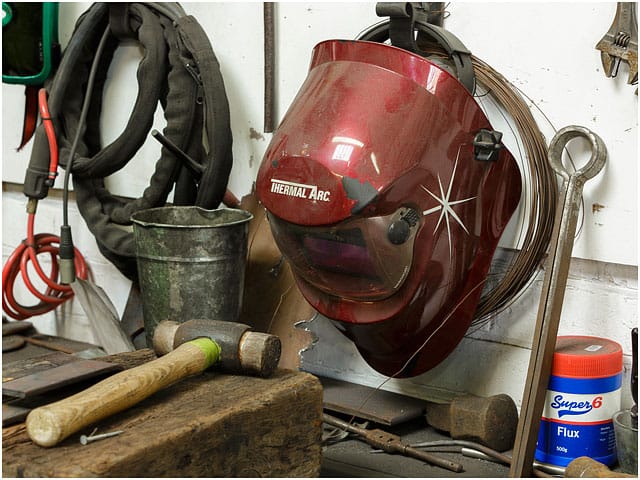 Blacksmiths workshop red welding helmet and tools hanging on wall Blacksmiths Workshop Red Welding Helmet And Tools Hanging On Wall