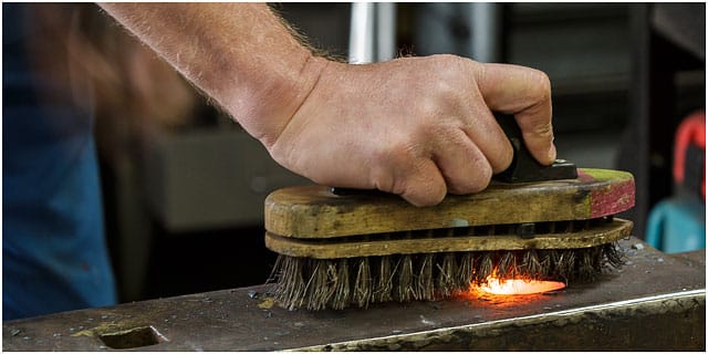 Removing Excess Scale On Red Hot Poker On A Blacksmiths Anvil With Wire Brush