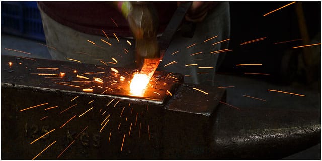 Hammering metal on anvil with flying sparks Hammering Metal On Anvil With Flying Sparks