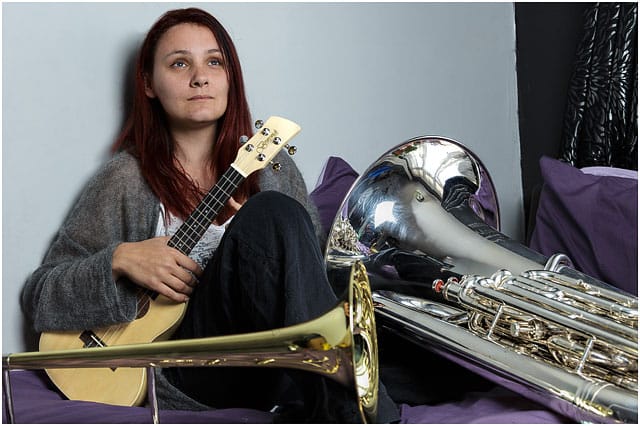 Female Brass Band Player Surrounded By Instruments On Bed