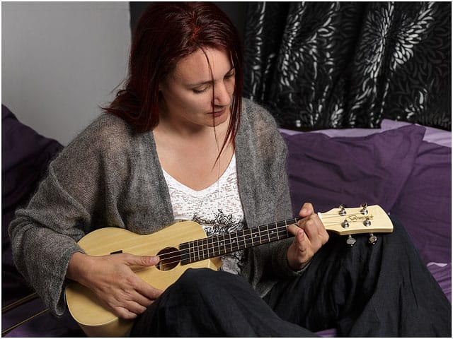 Female Ukulele Player Strumming Whilst Sat On Bed