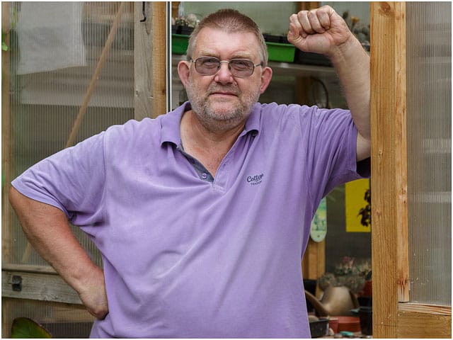 Portrait Of Man Leaning Against Door Of Handmade Greenhouse