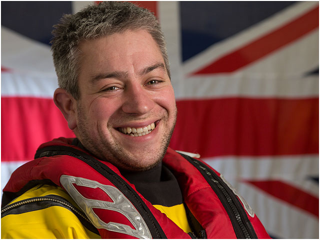 Head and Shoulders Portrait of RNLI Crew Volunteer with White Ensign Flag in Background