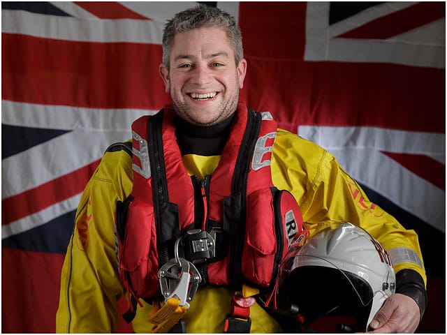 Head and Shoulders Portrait of RNLI Crew Volunteer with White Ensign Flag in Background