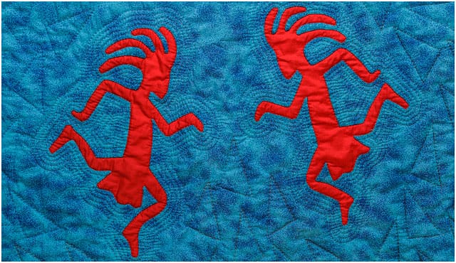 Red Quilted Kokopelli Figures On Blue Background 