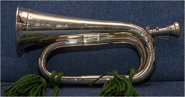 Brass infantry bugle with green tassels laying on a blue upholstered seat