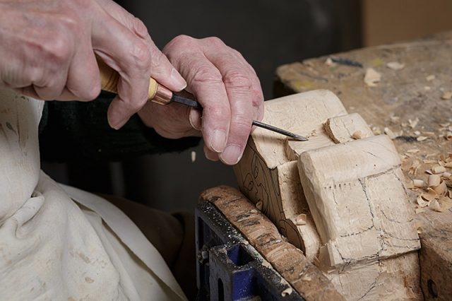 close up of woodcarvers hands working on a gargoyle carving 