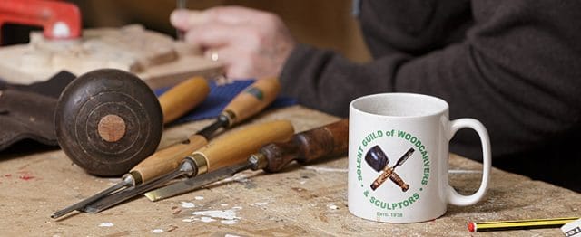 Solent guild of woodcarvers and sculptors coffee mug on bench with tools 