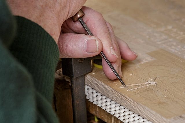 close up of woodcarvers hands carving gothic lettering 