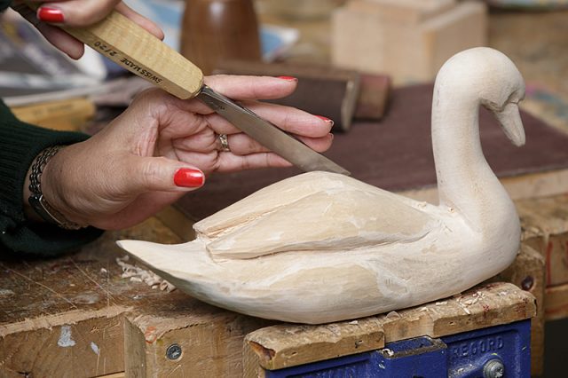 close up of female woodcarver carving a swan with a wood chisel 