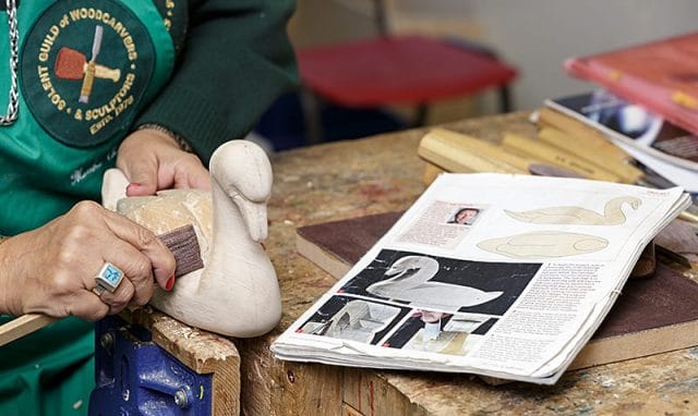 female woodcarver carving a swan with printed reference magazine in the foreground 