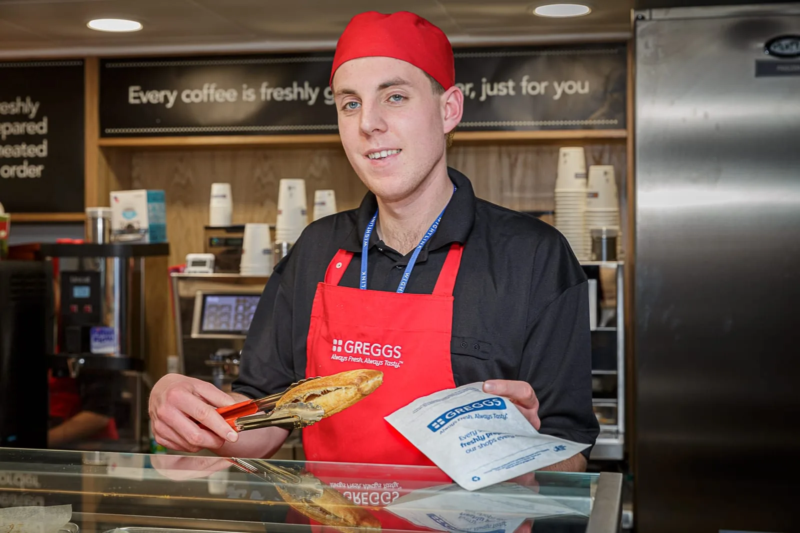 marketing portrait of a young man serving pastries at a counter wearing a branded uniform