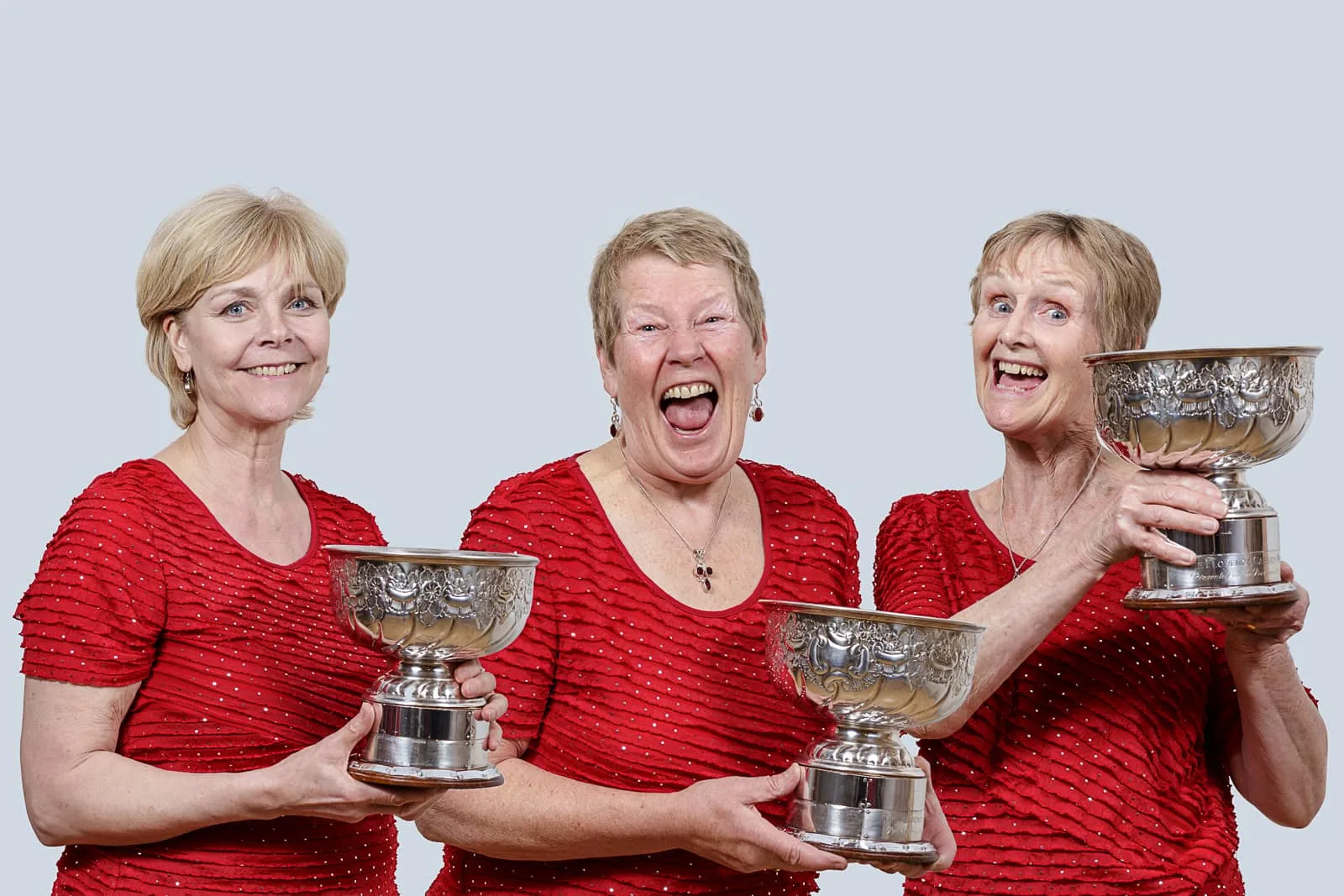 promotional portrait of three middle aged ladies holding celebratory singing award chalices