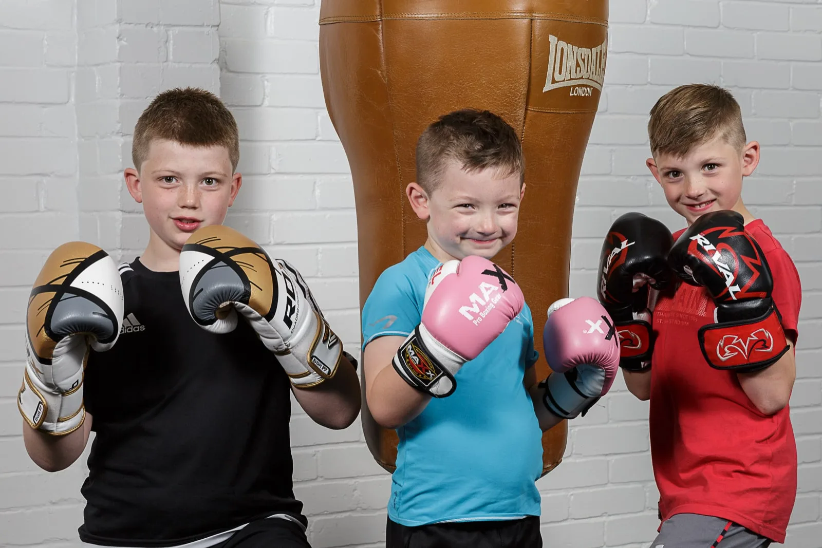 portrait of three young boys striking a boxing pose wearing boxing gloves with a punch bag