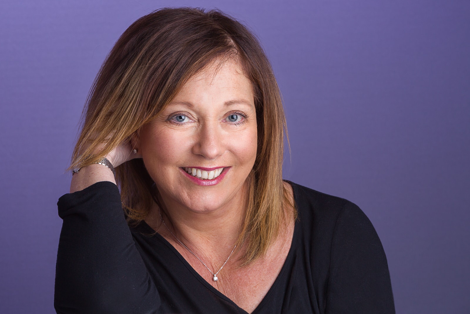 Marketing portrait of a middle aged woman with a dark top against a purple background
