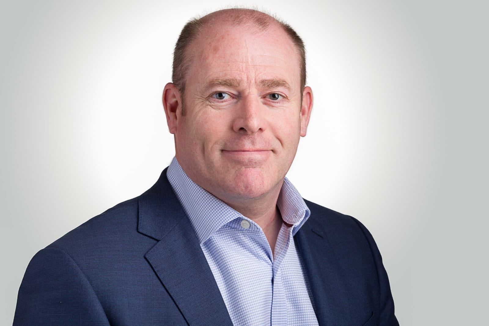 headshot of middle aged business man wearing blue jacket and open necked blue and white checked shirt