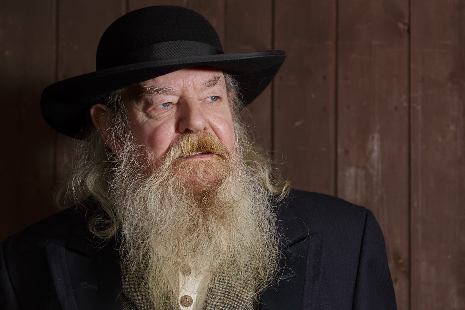 portrait of an older man with long light coloured beard wearing a black preachers hat and coat