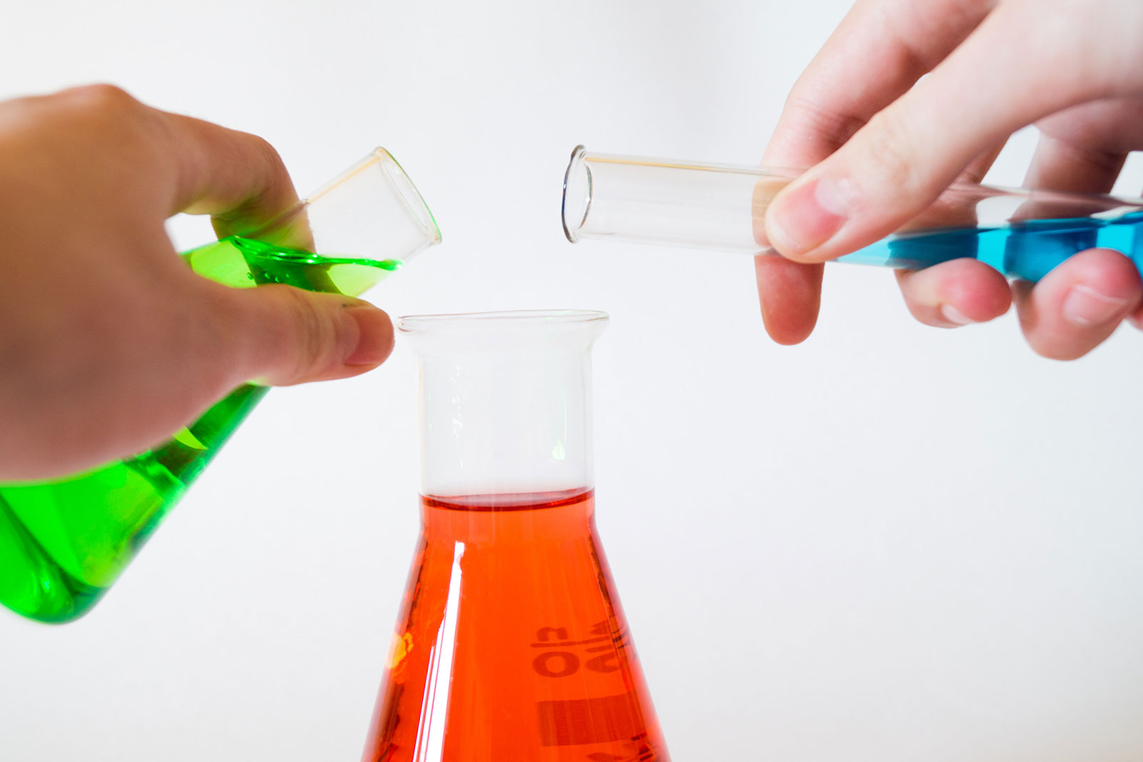 hands pouring liquids into glass flasks during a chemistry experiment
