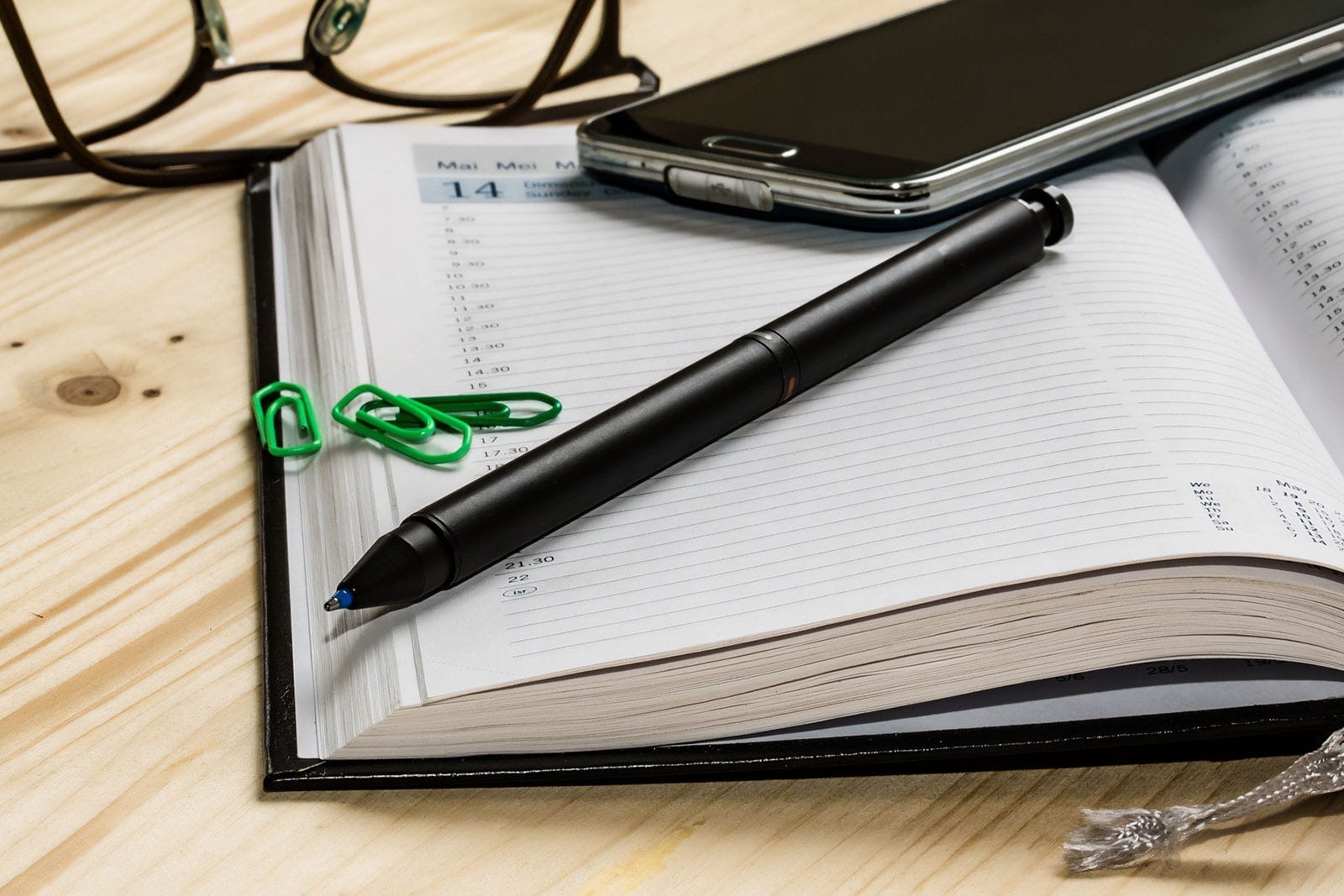 open diary pen mobile phone spectacles on desk