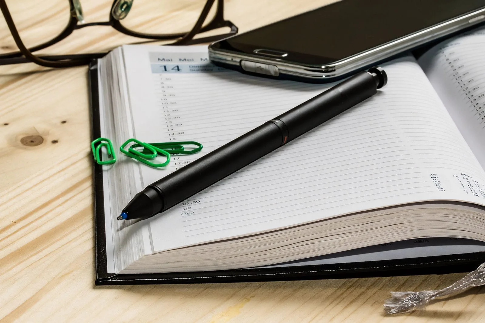 personal diary open on desk open diary pen mobile phone spectacles on desk