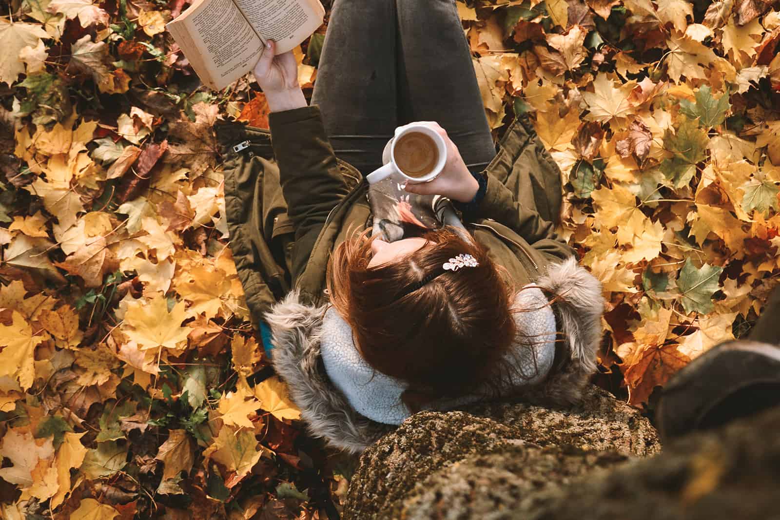 woman drinking coffee under a tree reading a book seen from above